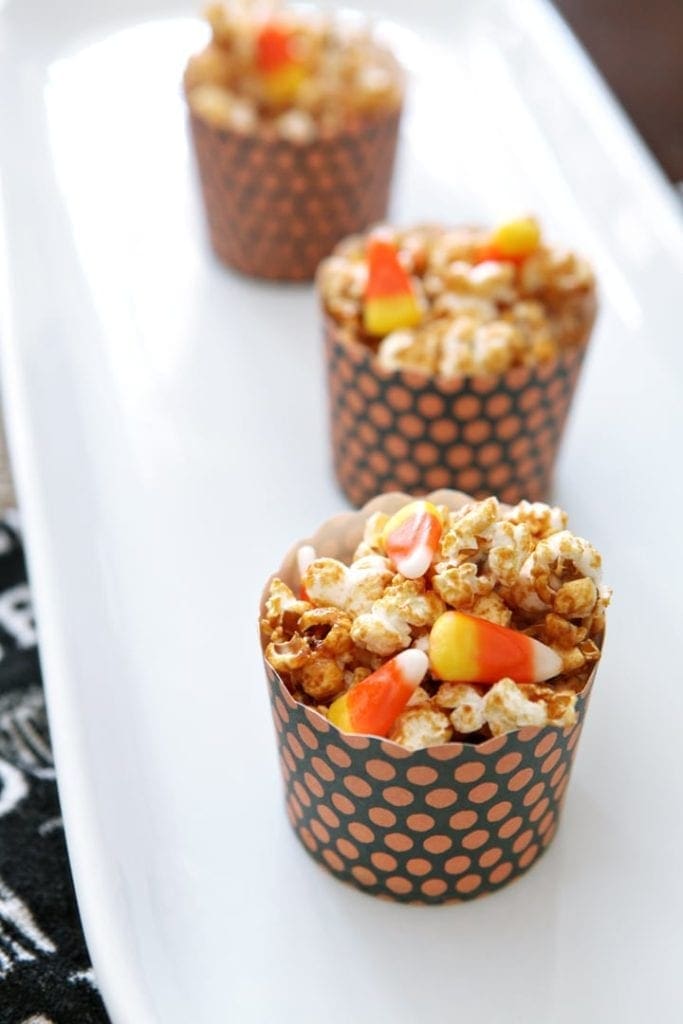 Three bowls filled with popcorn and candy corn on white plate 