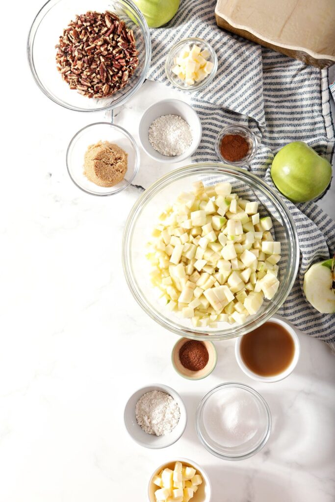 Ingredients to make apple crumble in bowls on marble with a blue striped towel