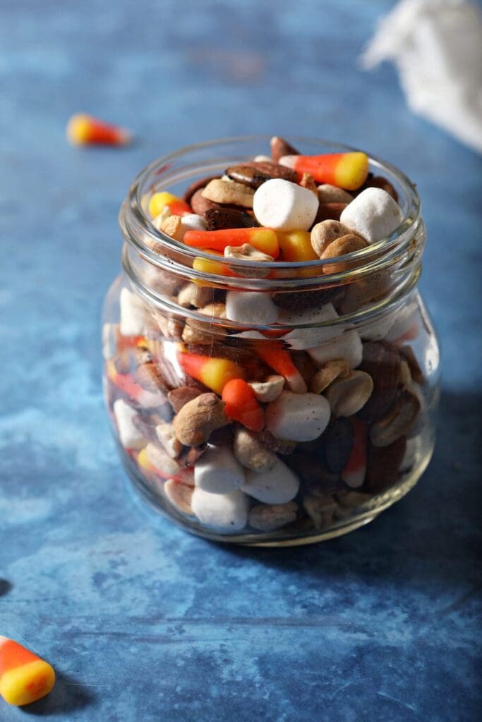 Halloween trail mix with candy corn in a mason jar on a blue background