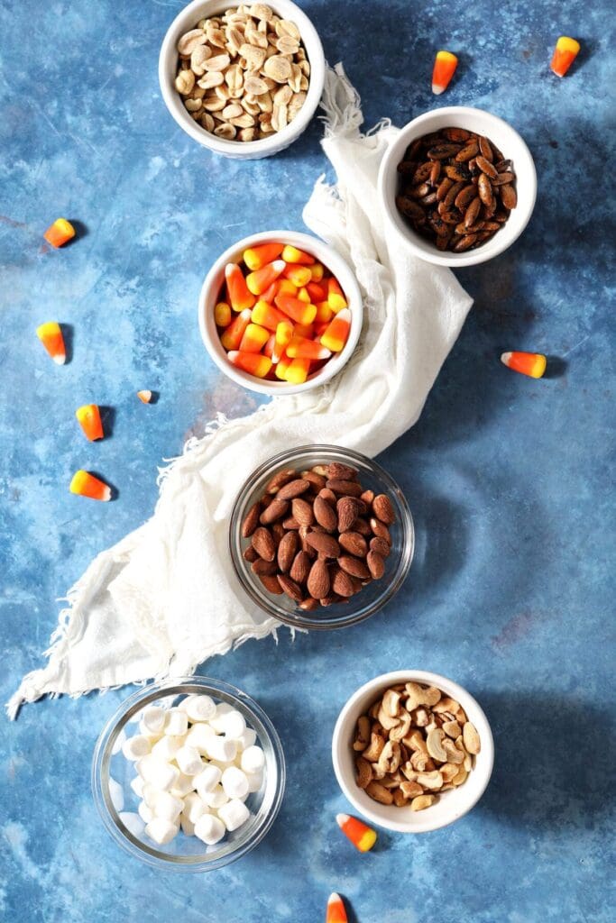 Bowls of nuts, candy corn and marshmallows with a white napkin on a blue background