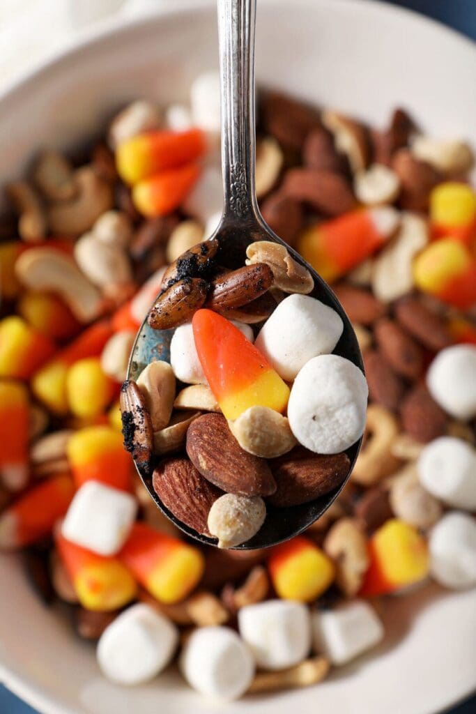 A spoon holds a bite of halloween trail mix above a bowl holding more