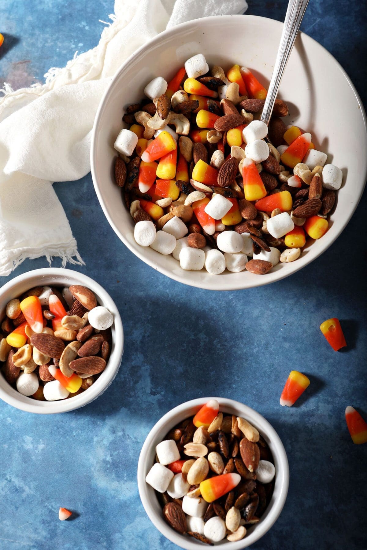Two small bowls and one larger bowl of Halloween trail mix on a blue surface
