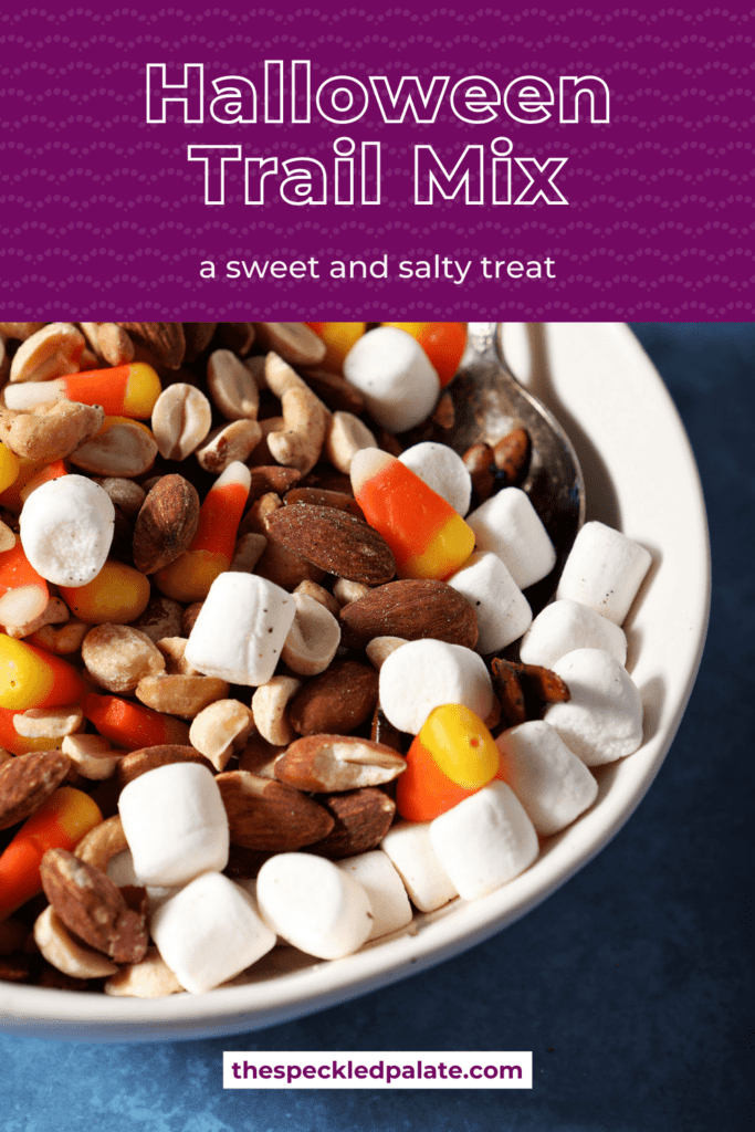 A spoon sits inside a bowl of nutty trail mix with candy corn and marshmallows with the text halloween trail mix a sweet and salty treat