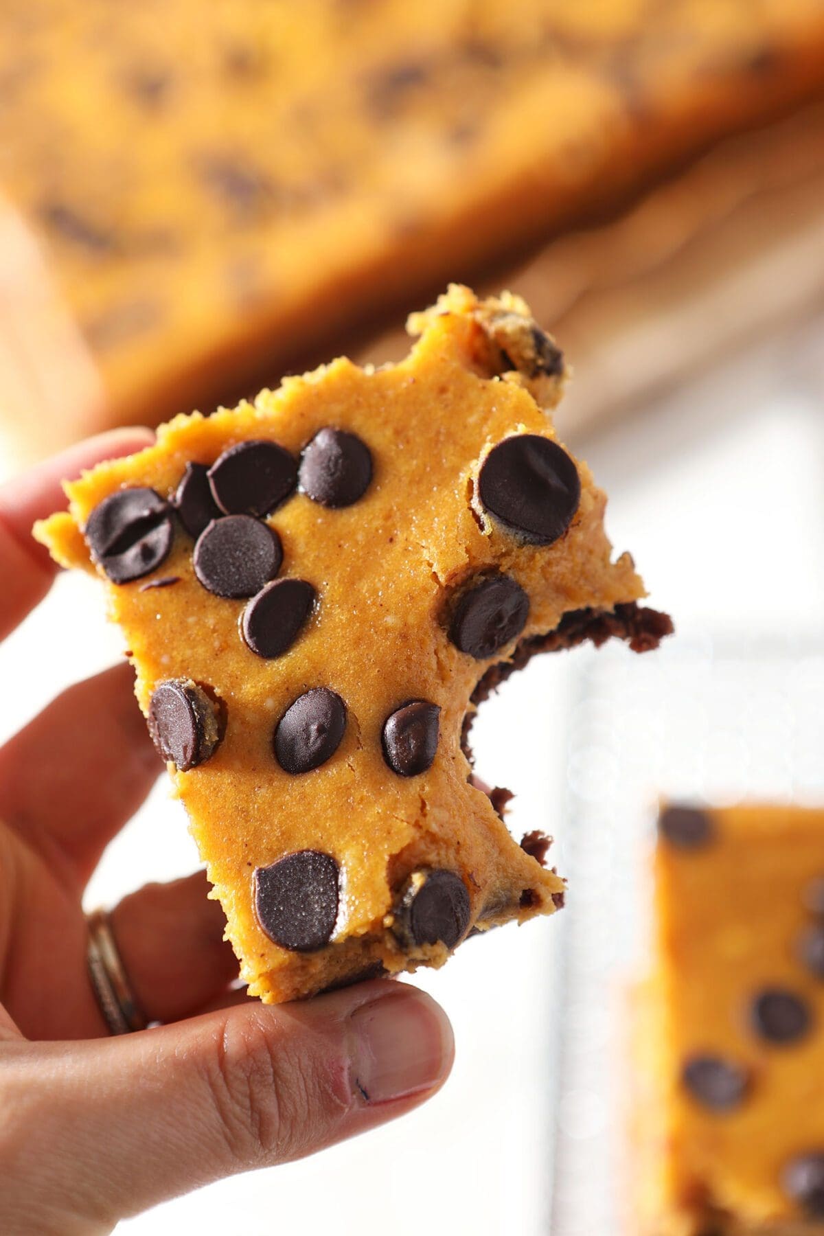 A bitten into Pumpkin Cheesecake Brownie Bars being held in hand above the rest of the bars