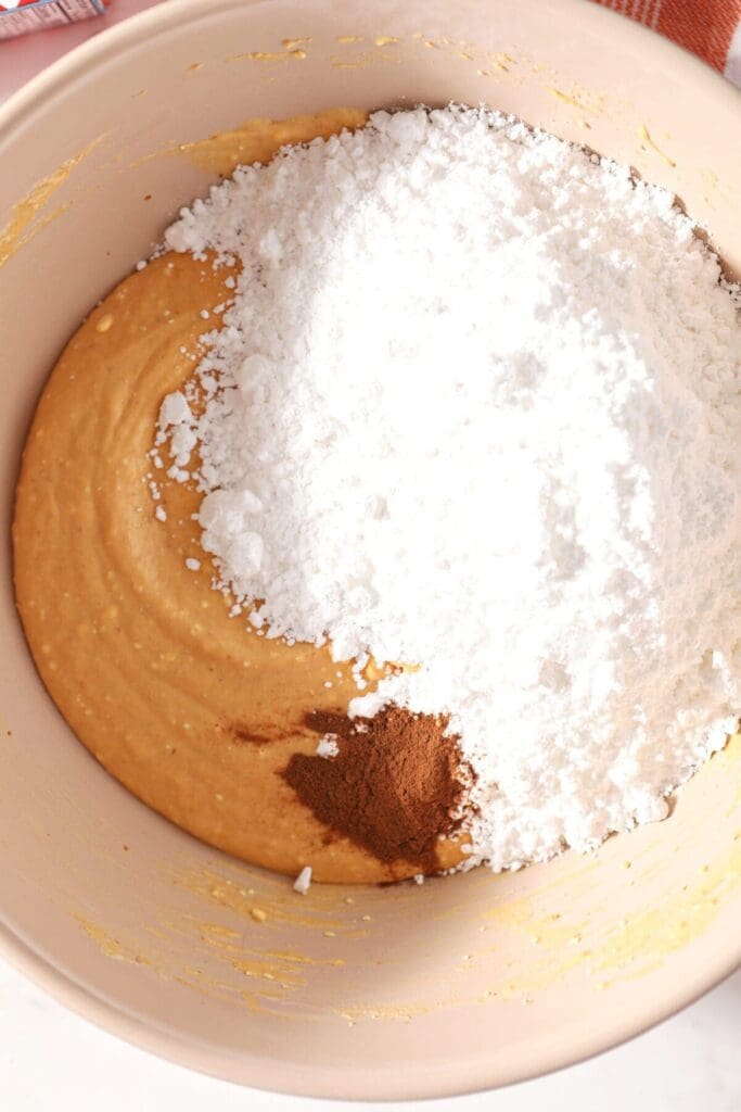 Powdered sugar and vanilla extract sit on top of a pumpkin-cream cheese mixture in a bowl