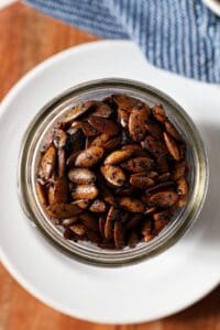 Close up of roasted pumpkin seeds in a mason jar on a white plate with a blue towel