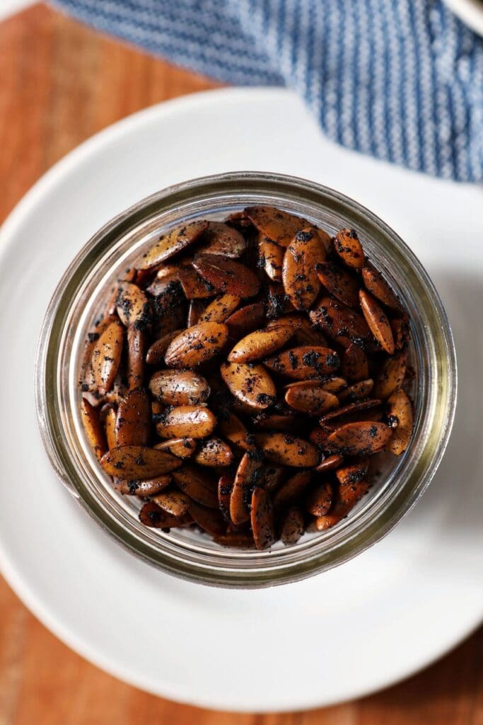 Close up of roasted pumpkin seeds in a mason jar on a white plate with a blue towel