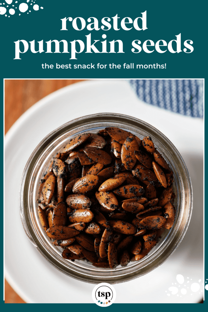 Close up of roasted pumpkin seeds in a mason jar on a white plate with a blue towel with the text roasted pumpkin seeds the best snack for the fall months