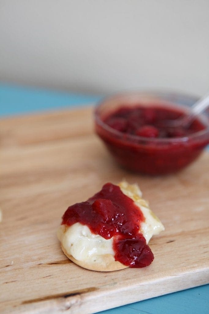 A bite of Baked Brie with Cranberry Chutney sits on a wooden cutting board