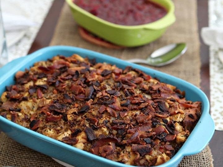 Stuffing in blue baking dish in front of Thanksgiving side dishes on wood board