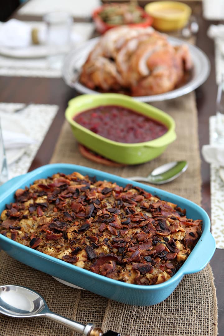 Stuffing in blue baking dish in front of Thanksgiving side dishes on wood board 