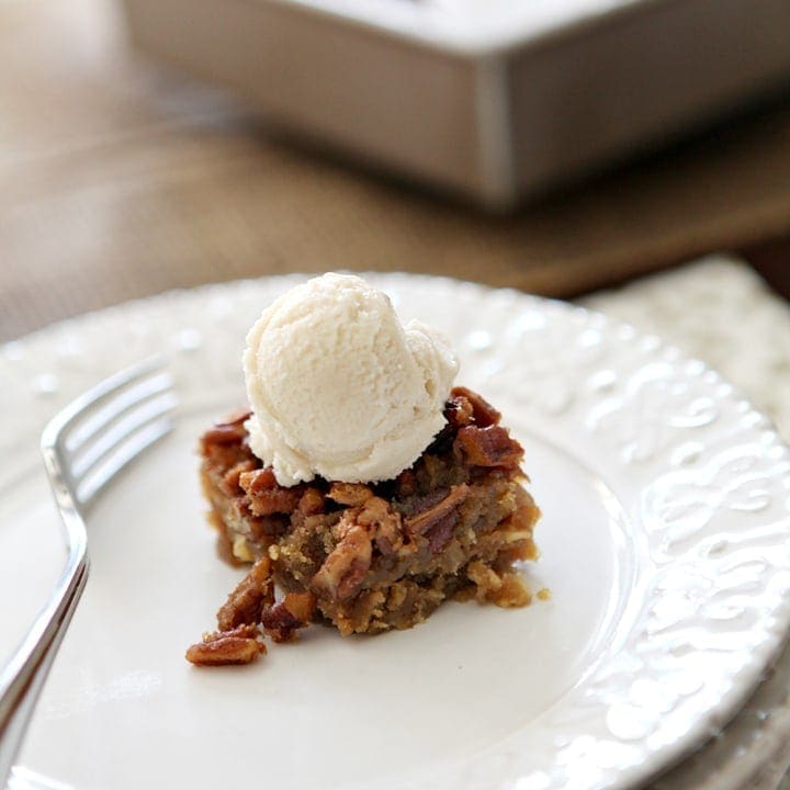 A Drunken Pecan Pie Bar sits on a white plate with the baking dish in the background