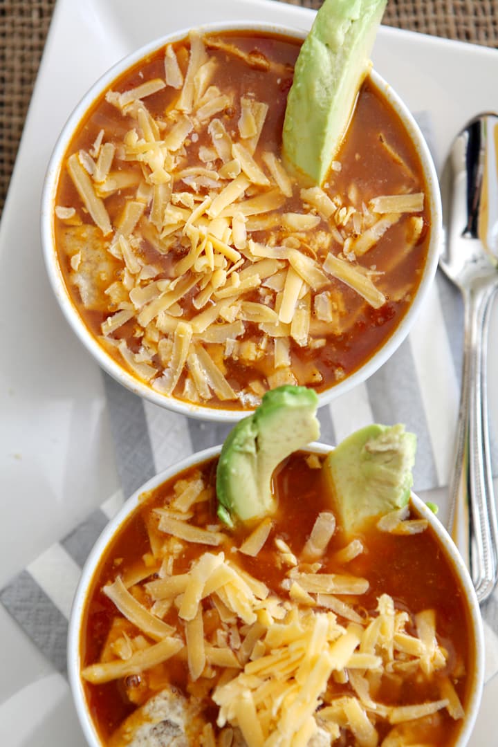 Overhead view of two bowls of turkey tortilla soup with shredded cheese and avocado 