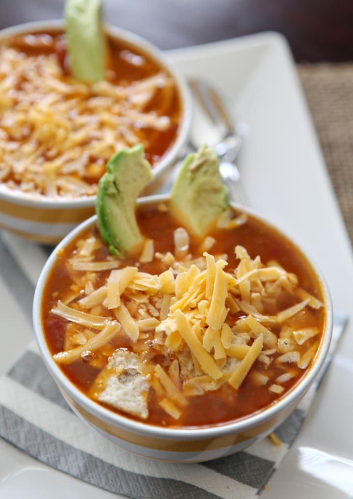 Two bowls of turkey tortilla soup with shredded cheese and avocado garnish 