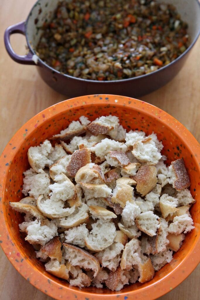 Torn up bread pieces in an orange bowl next to a dutch oven of cooked down veggies