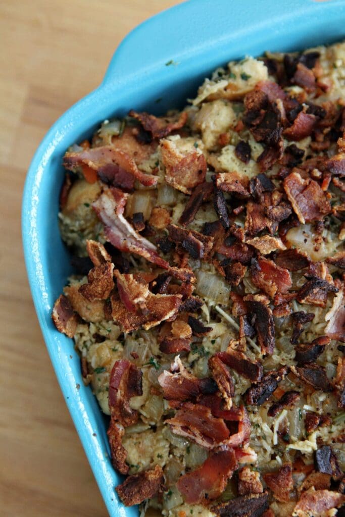 Stuffing with bacon on top of it in a blue casserole dish before baking