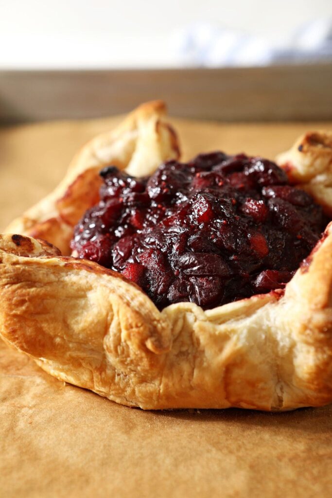 Baked Brie in Puff Pastry with Cranberry Chutney is a creamy, gooey appetizer for any holiday celebration. Topped with a tart, spiced Cranberry Chutney before it bakes, this Puff Pastry Baked Brie is a decadent recipe that looks fancy but is actually quite simple to make! Enjoy the extra cranberry chutney served alongside your meal, too!

Baked Brie topped with cranberry chutney and wrapped in puff pastry sits on a parchment-lined sheet pan after baking