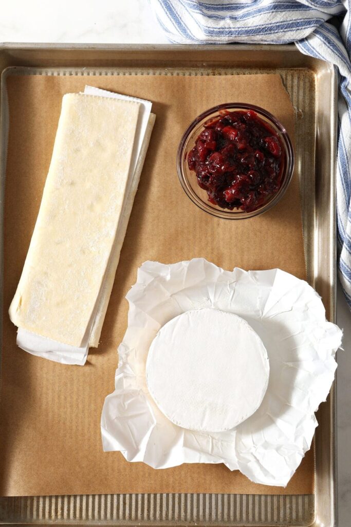 Ingredients to make Baked Brie in Puff Pastry with Cranberry Chutney on a parchment-lined sheet pan