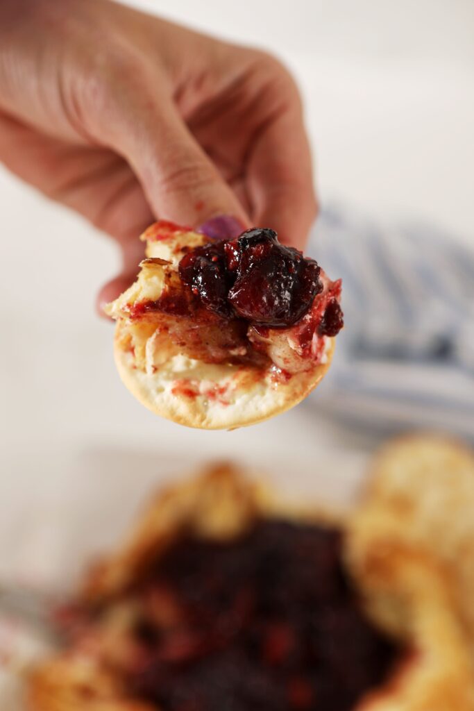 A hand holds a cracker slathered with Baked Brie and cranberry chutney