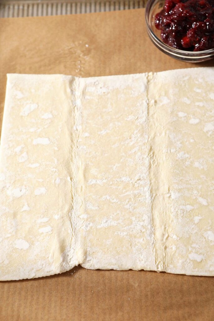 A sheet of puff pastry is flattened on a parchment-lined sheet pan