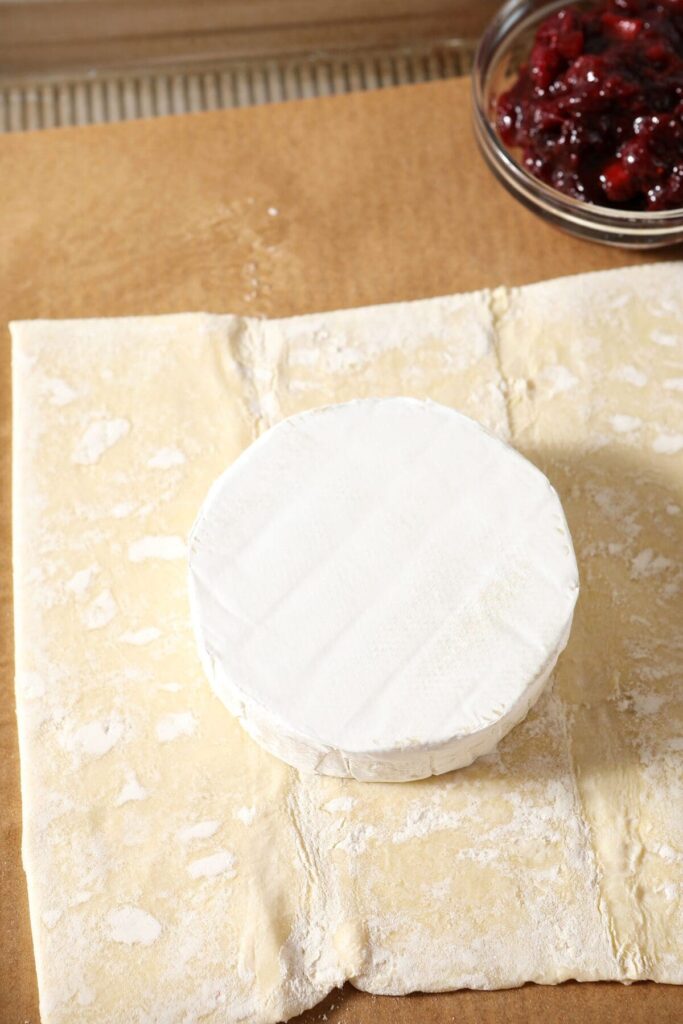 A wheel of brie sits inside a flattened piece of puff pastry