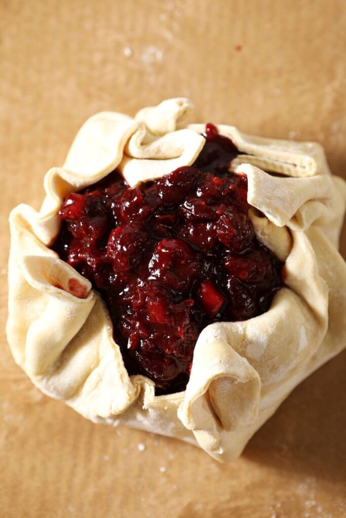 Puff pastry swaddles a wheel of brie topped with cranberry chutney before baking on a parchment lined sheet pan