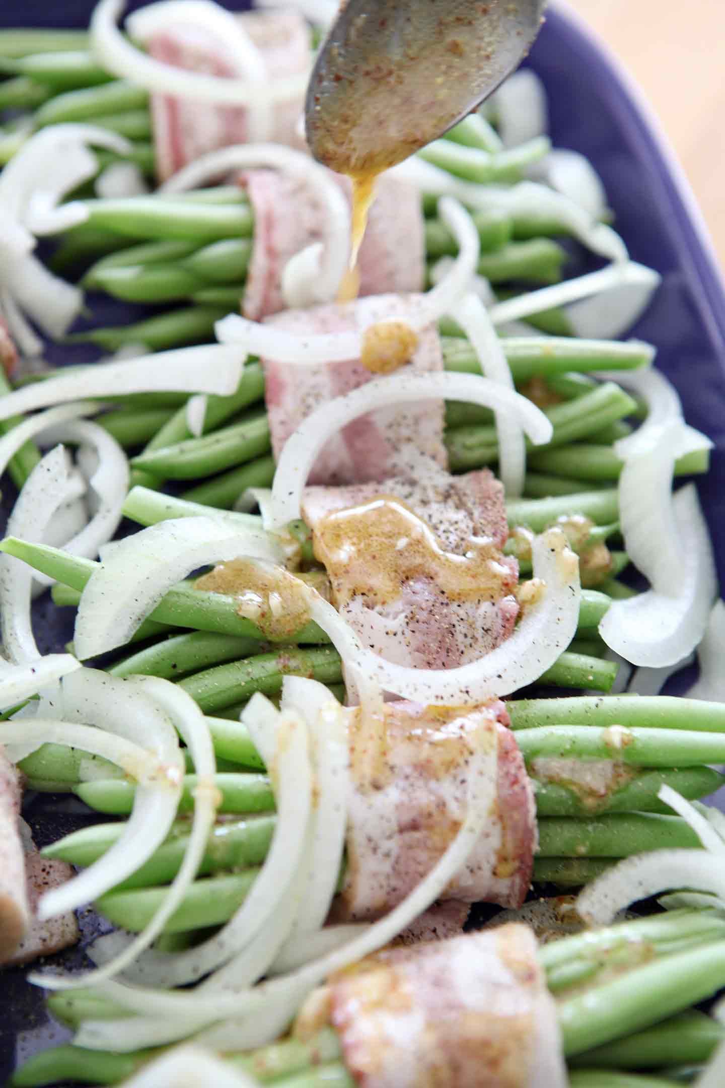 Green Bean Bacon Bundles are drizzled with sauce before baking