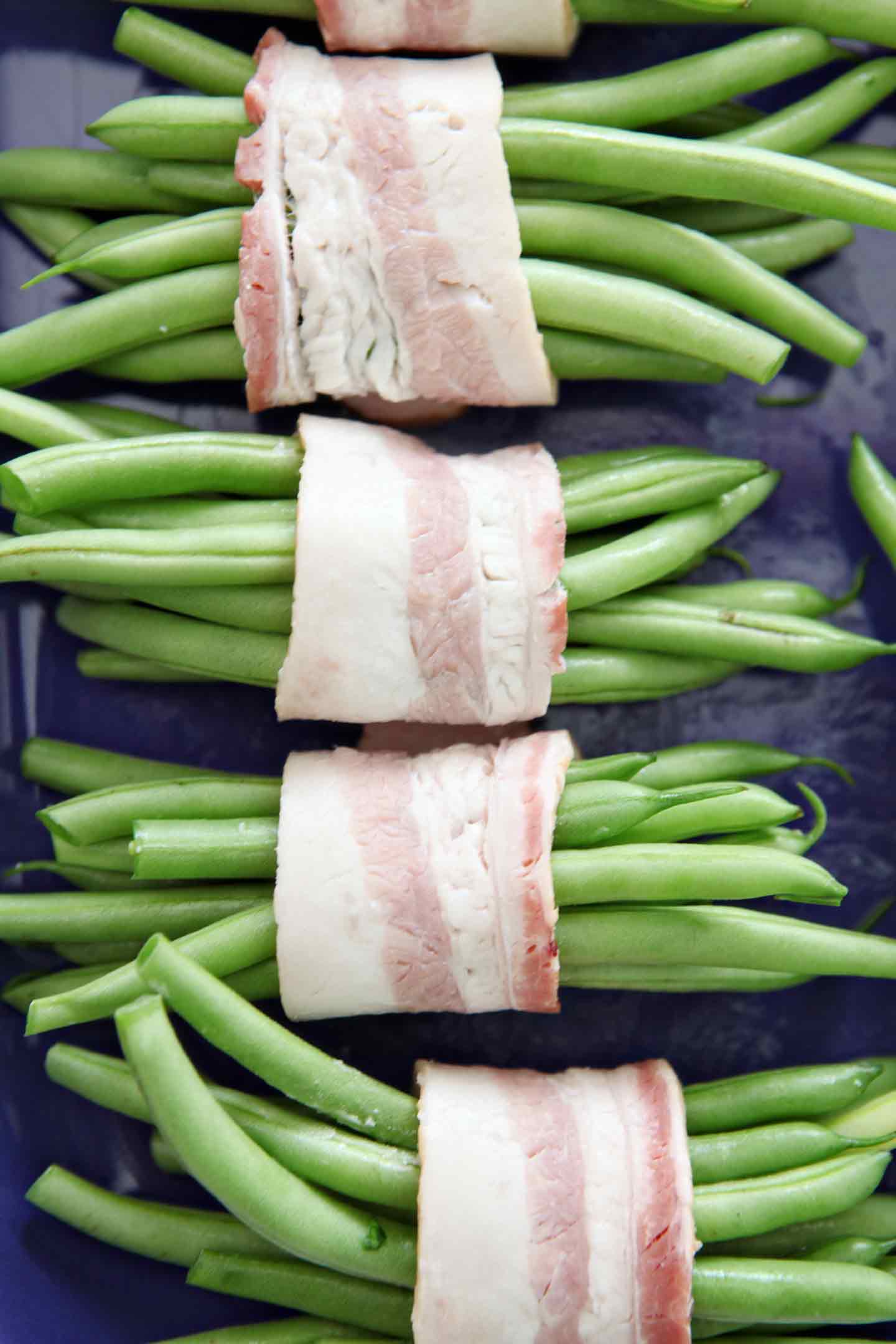 Close up of Green Bean Bacon Bundles in a purple baking dish before they are baked