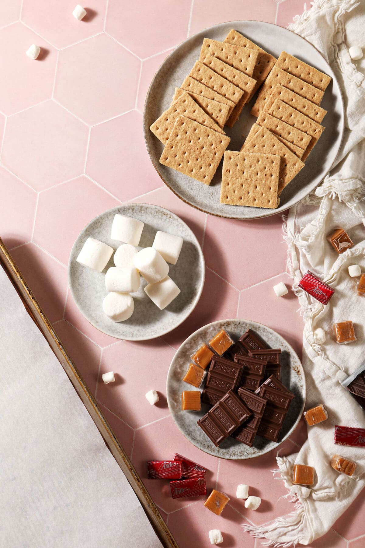 Ingredients to make indoor s’mores on plates on a pink tiled surface