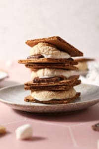 A stack of three baked s&rsquo;mores on a grey plate on a pink tiled surface