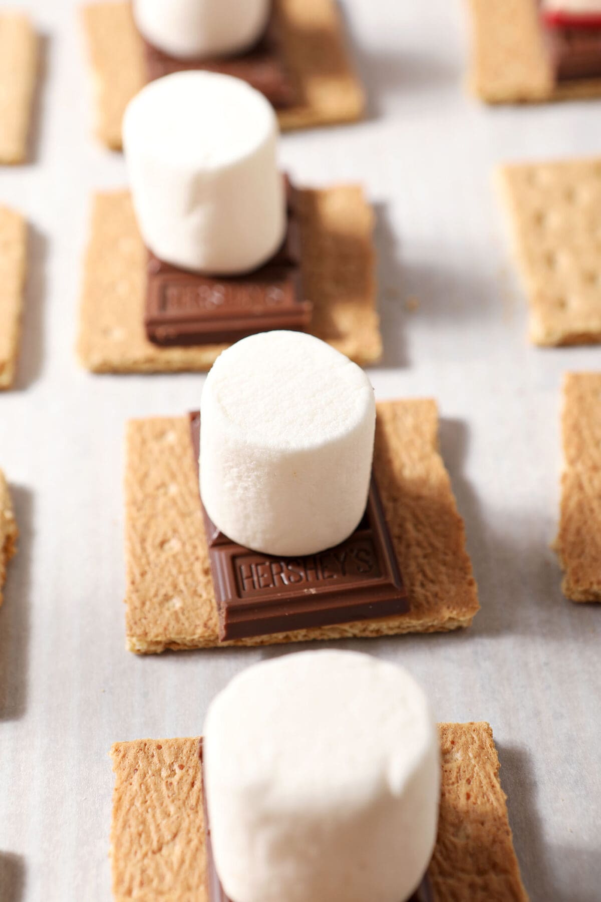 Marshmallows on top of chocolate bars on Graham crackers on a sheet pan