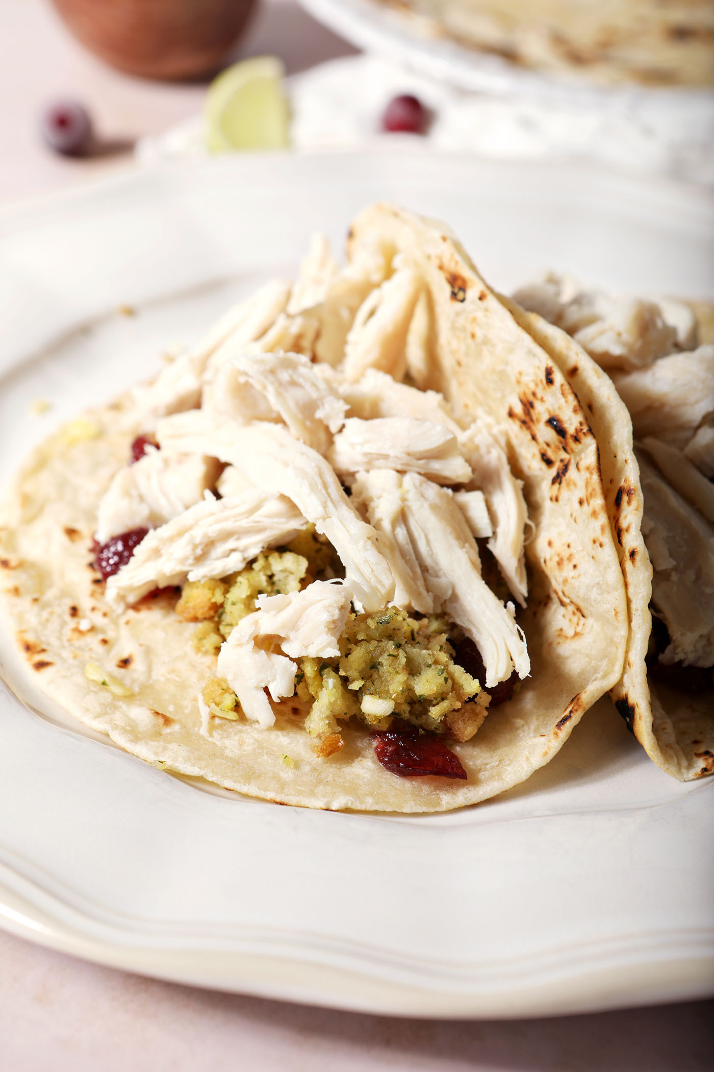 Shredded turkey on top of stuffing and cranberry sauce in a tortilla on a white plate