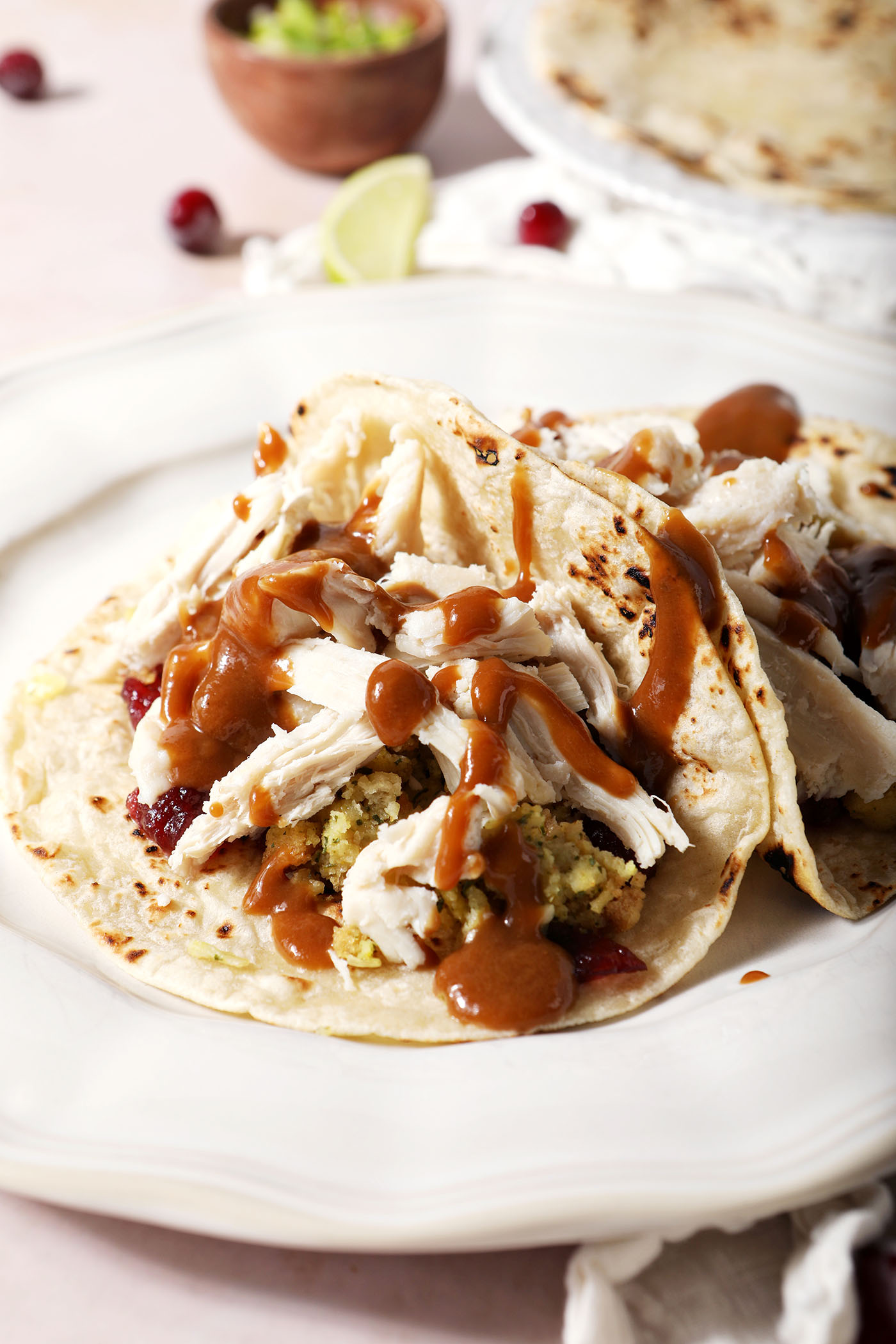 Gravy drizzled over shredded turkey, stuffing and cranberry sauce in a tortilla on a white plate