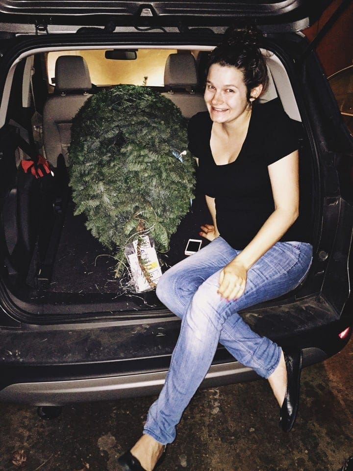 A woman sitting in the trunk of a car next to a christmas tree 