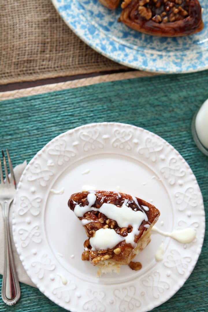 Icing drizzled on top of walnut sticky bun served on white plate 