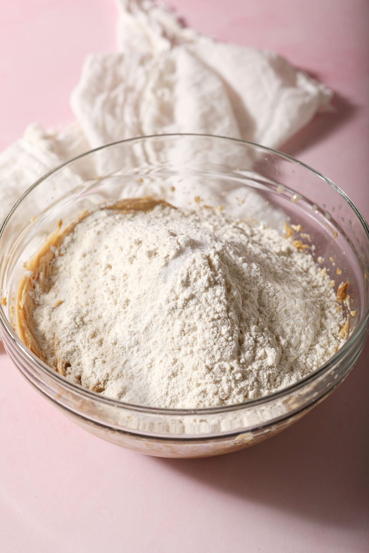 Flour and other dry ingredients on top of wet ingredients in a bowl on a pink countertop