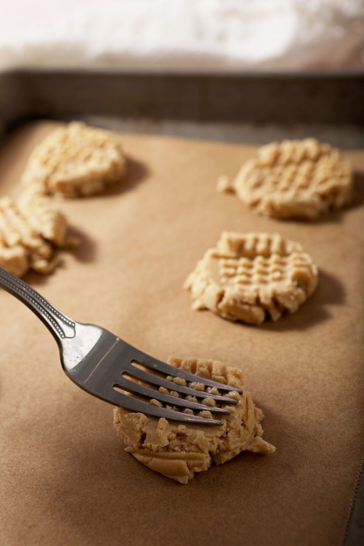 A fork makes cross marks on top of a shortbread cookie on a sheet pan