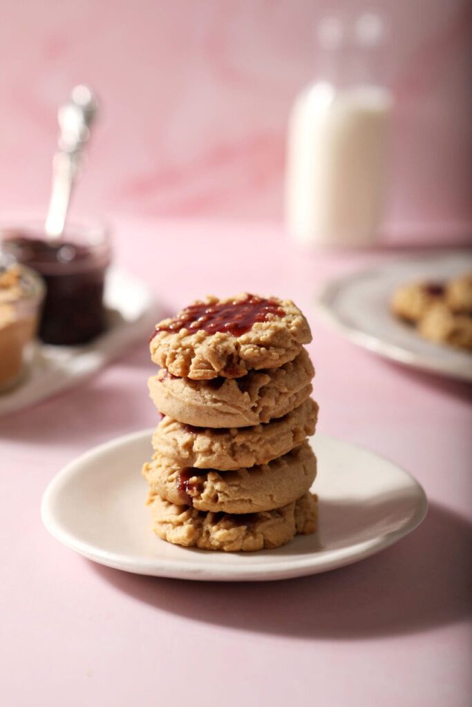 Stacked peanut butter shortbread cookies with raspberry glaze on a white plate on a pink countertop