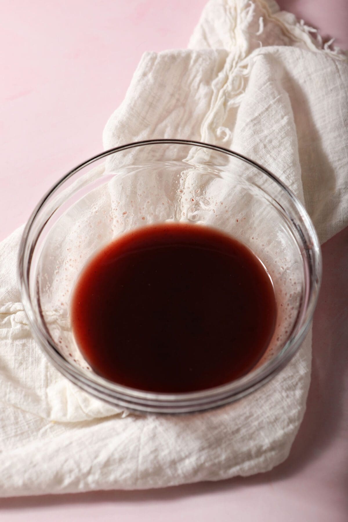 Raspberry-orange glaze in a bowl on top of a white towel on a pink countertop