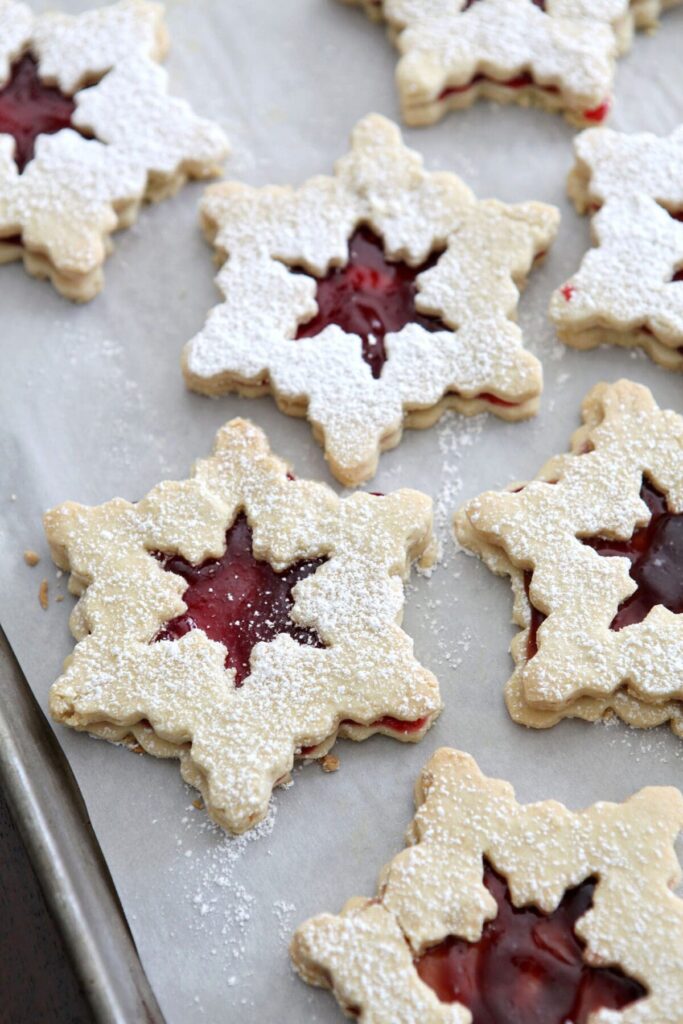 Snowflake-shaped raspberry liner cookies on a baking sheet