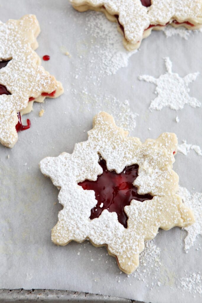 Three snowflake liner cookies on a sheet pan with powdered sugar