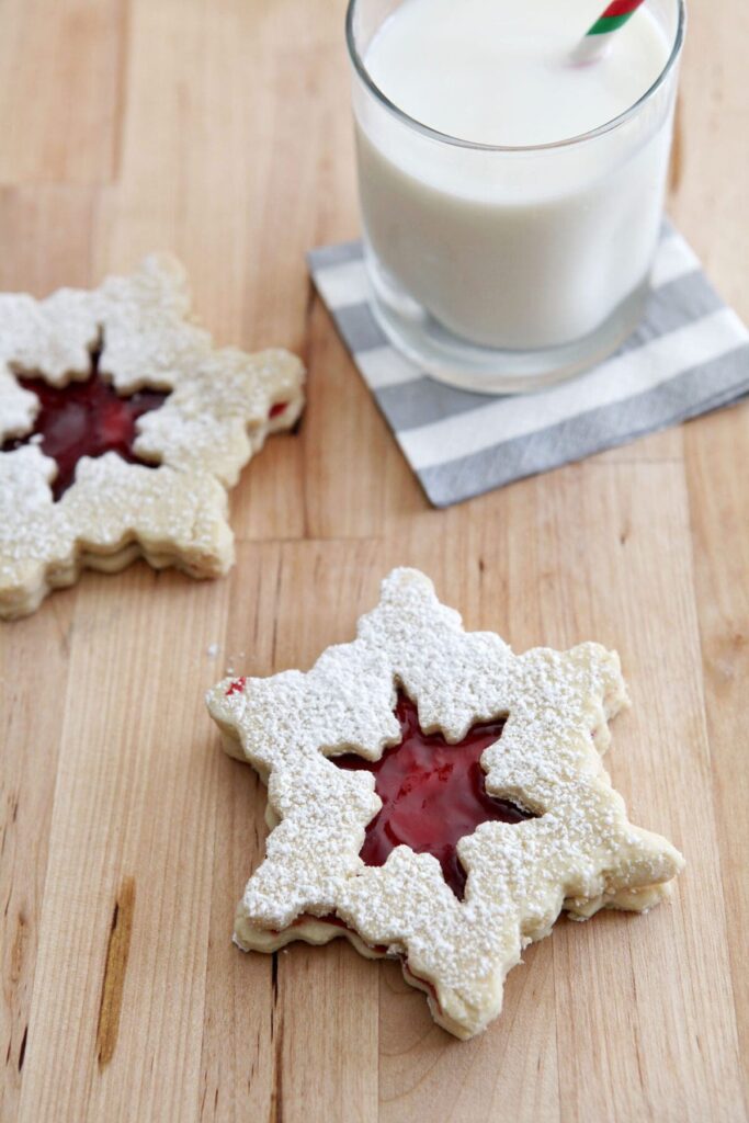 Two Raspberry Linzer Cookies on a wooden board with a glass of milk