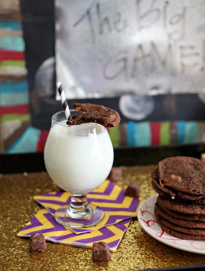 A Cookie sitting on top a glass of milk next to stack of cookies 