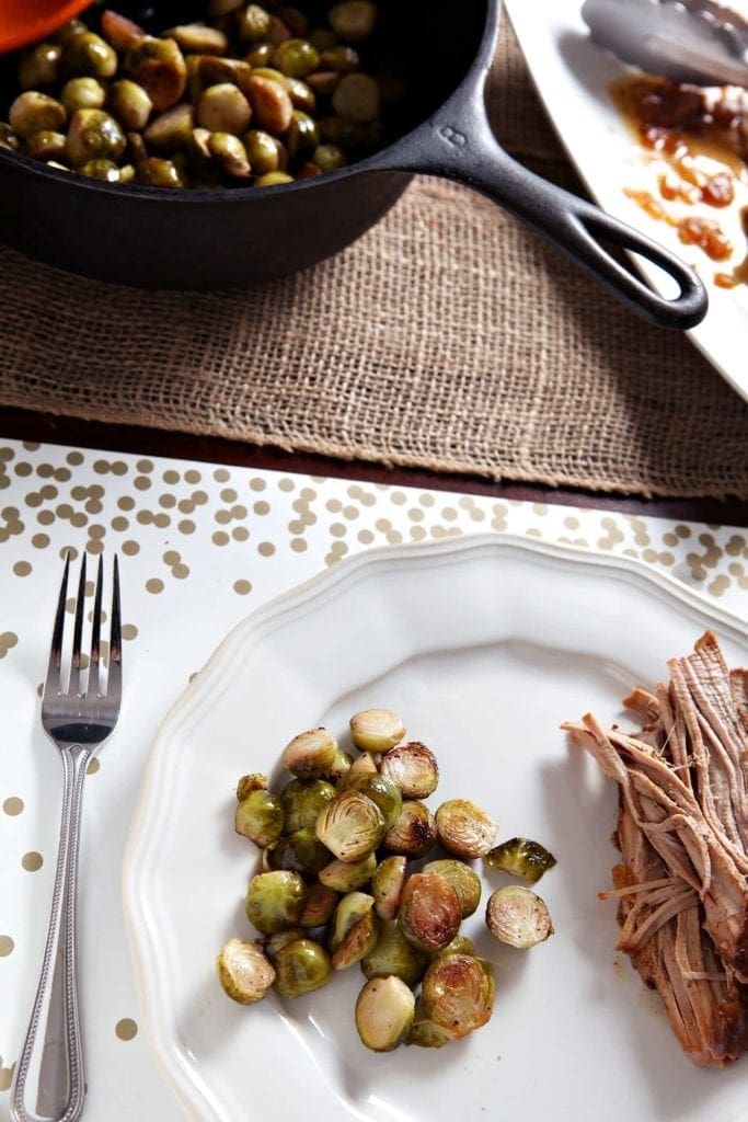 A serving of Lemon Brussels Sprouts on a white plate beside a serving of slow cooker pork tenderloin