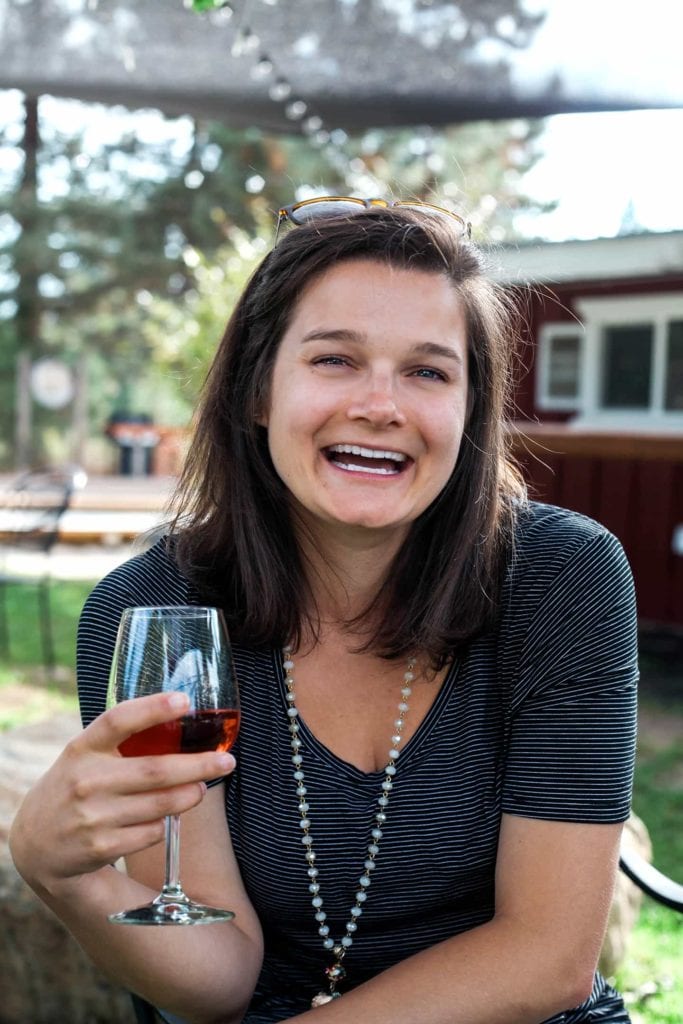 A woman sits beneath an awning, laughing while holding a glass of red wine