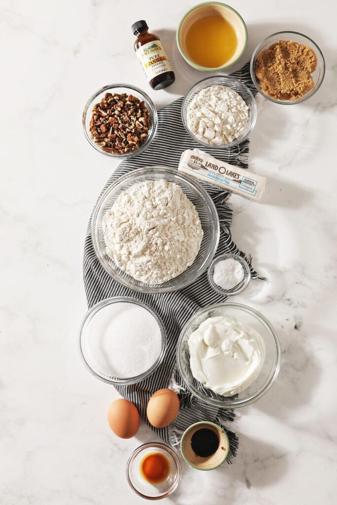 Ingredients for muffins sit in bowls on a marble countertop on top of a gray striped towel