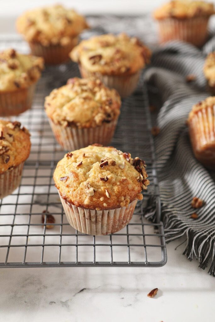 Coffee Cake Muffins sit on a wire cooling rack next to a gray striped towel