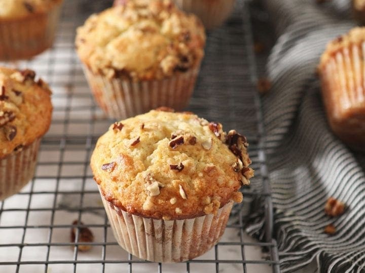 Coffee Cake Muffins sit on a wire cooling rack next to a gray striped towel