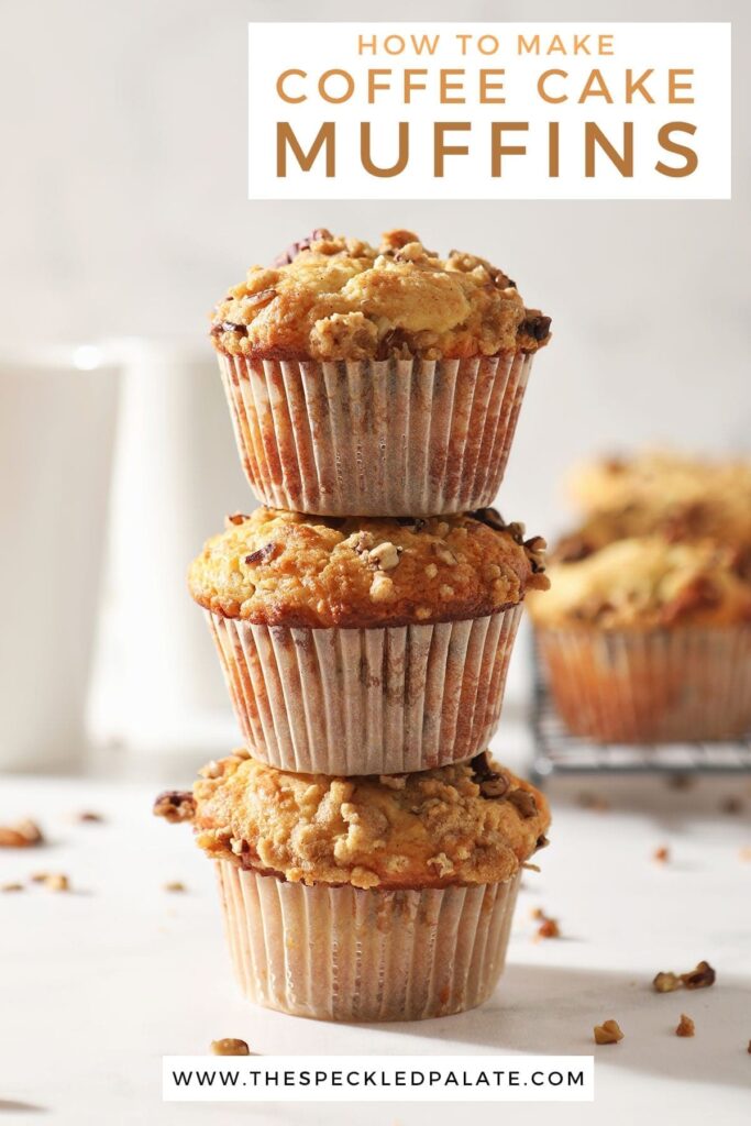 Three Coffee Cake Muffins are stacked on top of each other in front of a coffee mug and a wire cooling rack holding more muffins with the text 'how to make coffee cake muffins'