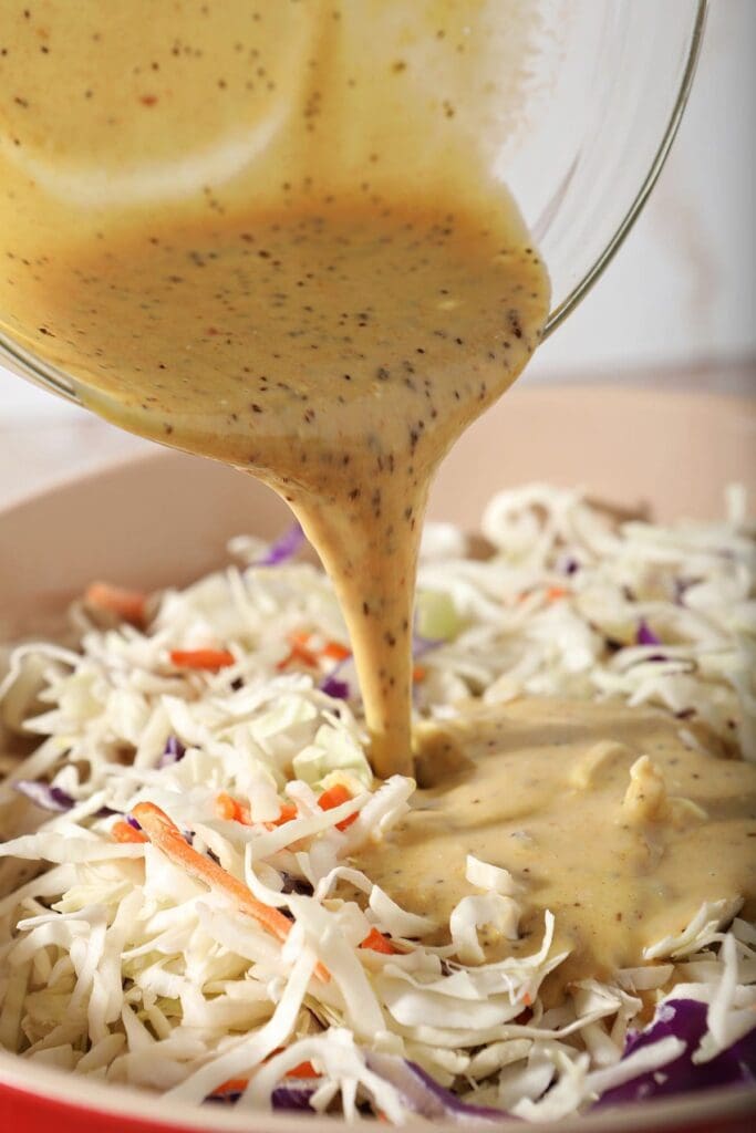 Coleslaw sauce pours on top of a cabbage mixture before tossing